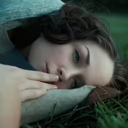 a woman resting in a field holding her chin on a pillow