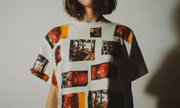 a woman stands in front of a white wall wearing a graphic shirt with photos on it