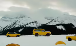 two cars with tents in the snow with mountains behind