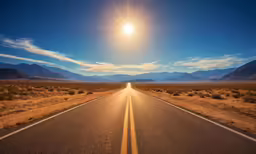 an empty road stretches into the sun in a desert landscape