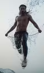 man jumps from water into the ocean with his shirtless head and flowing hair