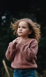 young girl standing in field with long hair blowing in the wind