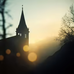 the clock is visible on this steeple in a foggy sunset