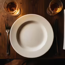 a table set with an empty plate, utensils and wine glasses