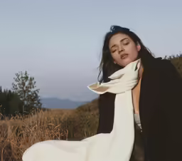 a woman wearing a white dress is sitting in a grassy field