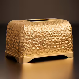 a gold colored rectangular shaped tissue box sits on a gold pedestal