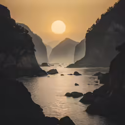 the sun sets over some rocks near a body of water
