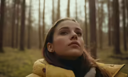 woman in yellow puffer jacket near forest looking up