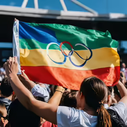 spectators holding an olympic flag and waving a sign
