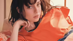 young woman in orange blouse with her arm on a pillow