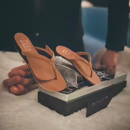 someone holding up their brown shoes on top of the shoe box
