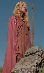 a woman in brown is standing behind a rock