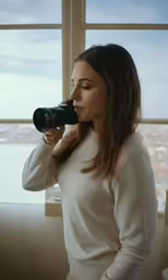 a woman is standing near a window taking a picture