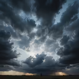 the silhouettes of clouds against a dark sky with the sun peeking over them