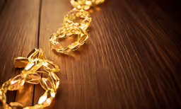 gold chain laying on wooden surface with light coming from them