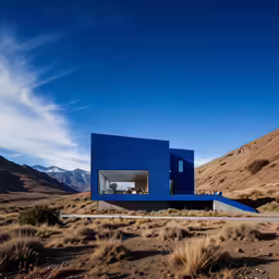 a blue building in the desert with mountains in the background