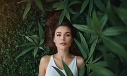 a woman standing under some greenery with her hair blowing back