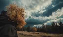 a man with red curly hair stands outside in a meadow