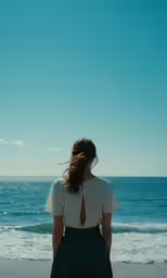 a woman is standing on the beach in front of the water