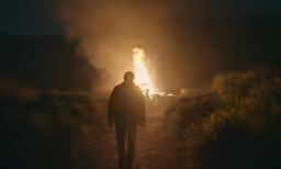 man walking down path by burning vehicle near large area