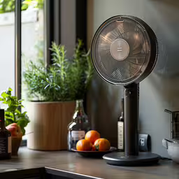a modern, portable fan is on a counter top,an old fan sitting on top of a counter next to some oranges