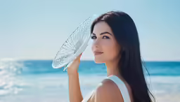 a woman holds a white hat up to her face as she looks at the water