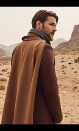 man in brown cape in desert area next to mountains