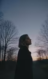 a woman stands in front of trees at dusk