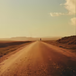 an unpaved dirt road surrounded by large hills and grasses