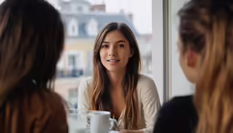 a woman sitting in front of a window talking to two other women