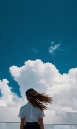 a woman standing in front of the clouds and looking up at the sky