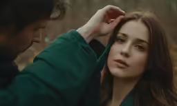 a man adjusting his hair next to a young woman in the woods