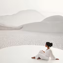 a woman sitting on a white surface next to mountains