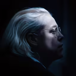 a woman wearing glasses and blond hair looks over her shoulder