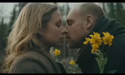 a woman kissing a man while standing next to yellow flowers