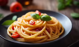 pasta with sauce and fresh basil leaves in a black plate