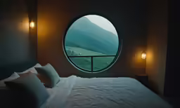 a bed sits in a dark bedroom under a round window