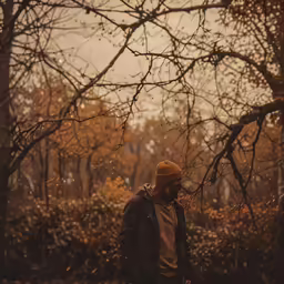 a young man in a hoodie and yellow hat stands under a tree