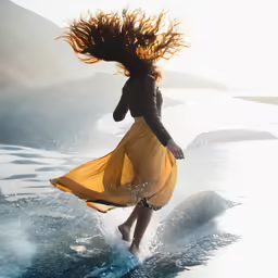 woman in a yellow dress running over water on the beach