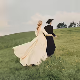 a man in a suit and a woman in a dress walking across a field