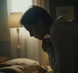 the woman is sitting on her bed holding her chest