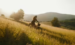 a girl riding her bike in a field near the trees
