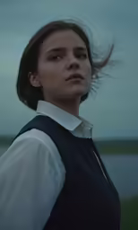 a girl standing outside by the water with her hair blowing in the wind