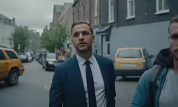 two men stand in the street, looking toward a yellow car