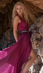 a pretty blonde in a purple dress standing by rocks