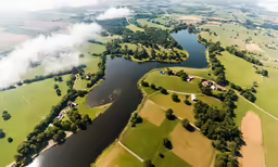an aerial shot of a river running between two green fields