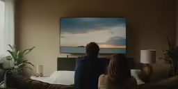 a man and woman sit on a couch in front of a television