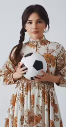 an asian woman in a floral print dress is holding a soccer ball