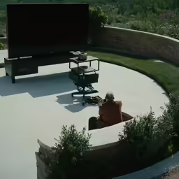 a man sitting in front of a giant screen outside