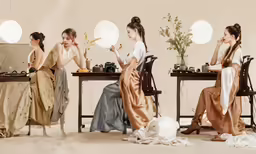 three women wearing brown dresses sitting at a table with two laptop computers